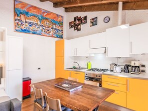 A modern kitchen with yellow cabinets, a wooden dining table, and a painting on the wall. - Aly d'angelo - im Turm by Interhome (Bardolino)