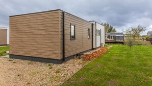 A modern mobile home with a wooden exterior, a small porch, and a garden area with gravel and grass.