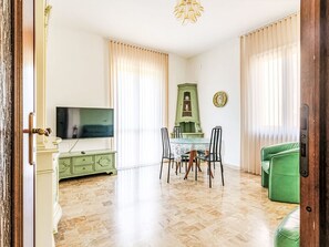 A living room with a television, dining table, chairs, a green cabinet, and a green sofa. - Wohnung 'Superior Apartment by Interhome (Albisola)