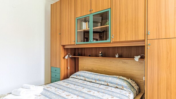 Una camera da letto con un letto in legno, un armadietto verde con ante in vetro e una piccola mensola con oggetti decorativi.