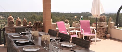 An outdoor dining area with wicker furniture, a stone pillar, and a view of the countryside.