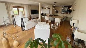 Una sala de estar moderna con muebles blancos, un comedor y una cocina.