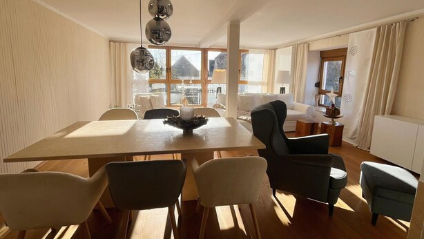 Un amplio comedor con una larga mesa y varias sillas, ventanas grandes que ofrecen luz natural y vistas al exterior.