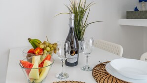 Une table à manger avec un saladier de fruits, une bouteille de vin et deux verres à vin.