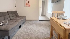 A modern living room with a grey sofa, a wooden dining table set with plates and cutlery, and a painting on the wall. - cozy one-bed apartment in the heart of Penzance (Penzance)