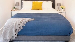 A bedroom with a bed, a nightstand, a lamp, a framed picture, and a carpet. - cozy one-bed apartment in the heart of Penzance (Penzance)
