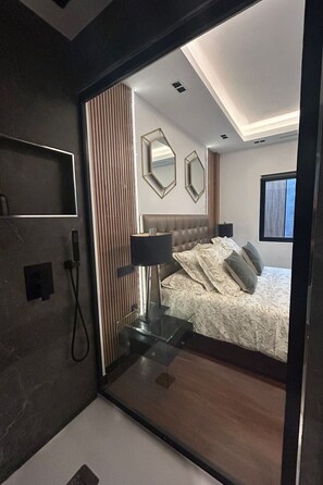 A modern bedroom with a large mirror, a bed with floral bedding, and a bedside table with a lamp. - Strand Canteras III by Interhome (Las Palmas)