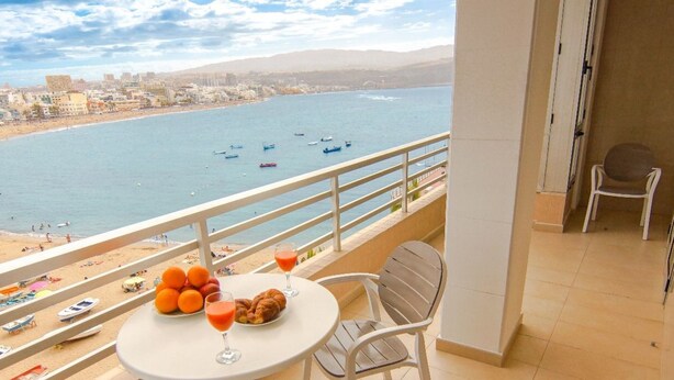 Ein Balkon mit Frühstückstisch, der auf einen Strand und das Meer blickt.