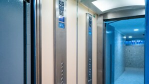 Ein Fahrgastaufzug mit metallischen Wänden, einer Handlauf und Bedienfeldern mit Knöpfen und Beschilderung.