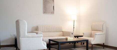 Una sala de estar moderna con un sofá color crema, dos sillones, una mesita de centro y una lámpara de pie.