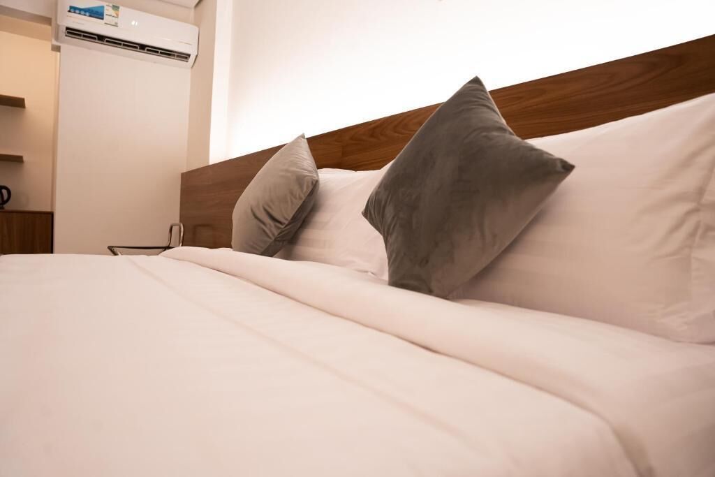A neatly made bed with white bedding and two pillows, a wooden headboard, and an air conditioning unit on the wall.