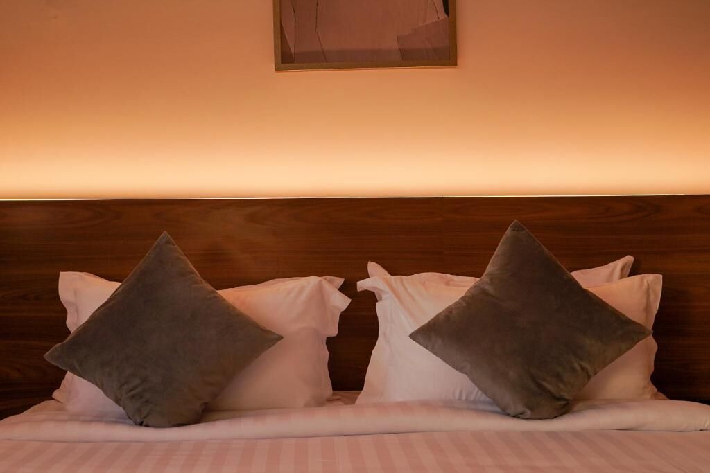 Una cama con cabecera de madera, dos almohadas y una manta blanca.