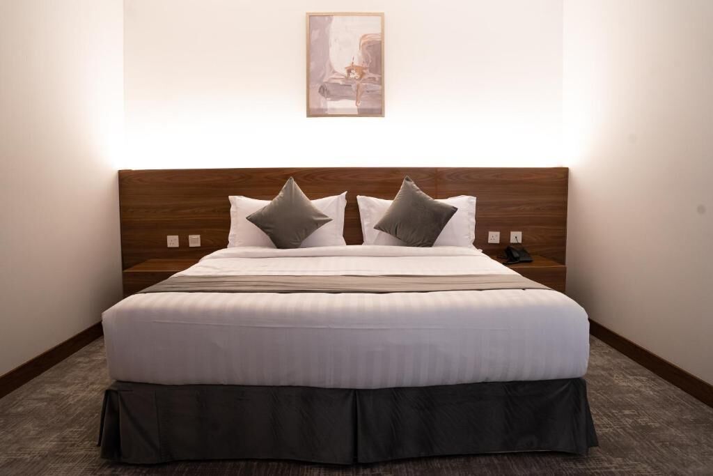Una cama bien hecha con cabecera de madera, dos almohadas y cubrepie oscuro.