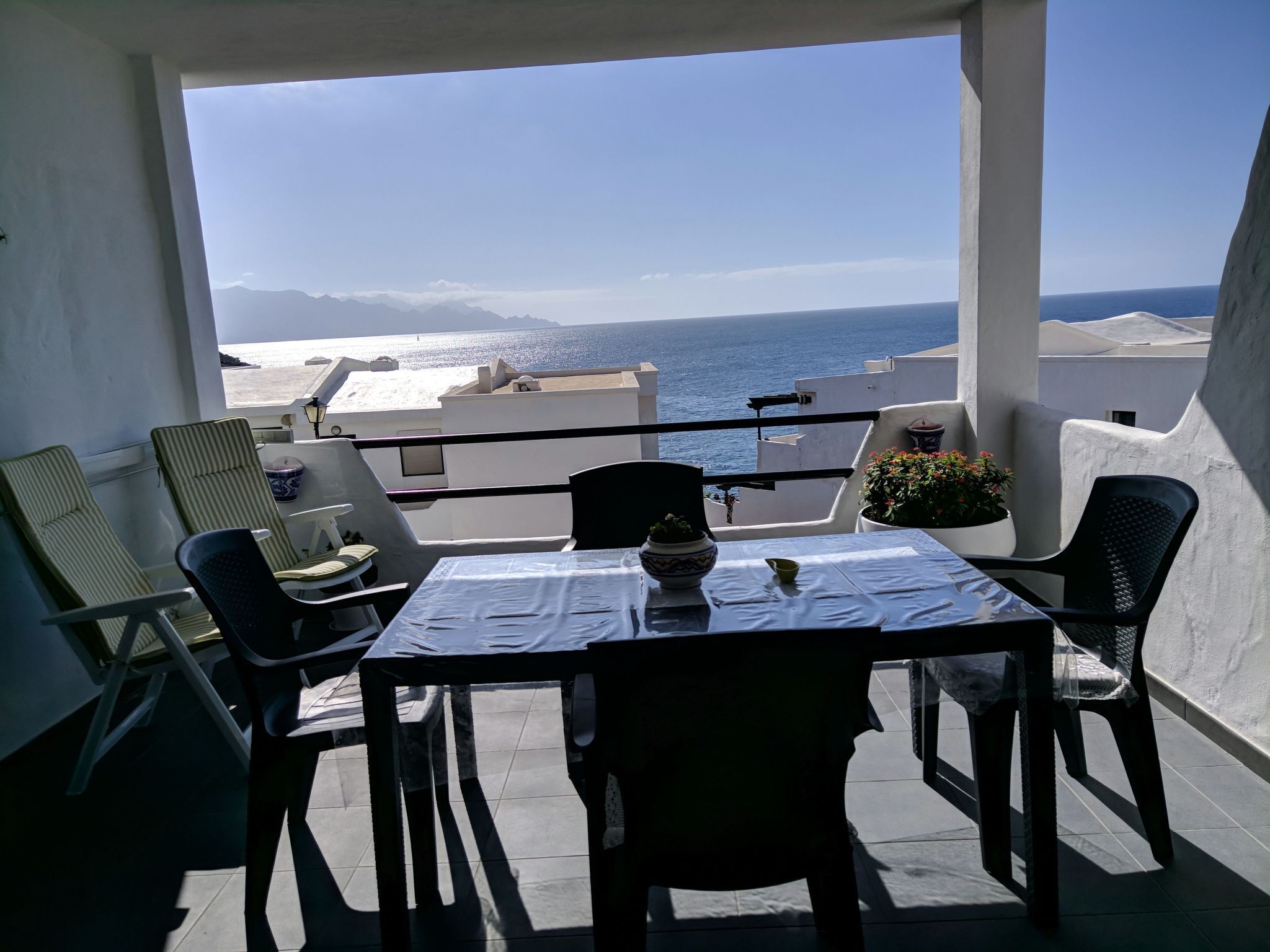 Een balkon met een tafel en stoelen, met uitzicht op de kust en bergen in de verte.