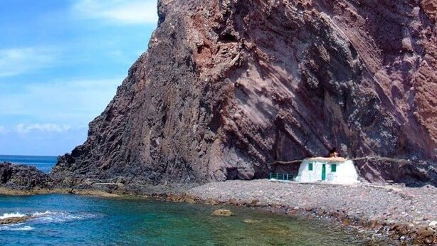 A rocky coastline with clear water and a small white building with a green door.