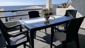 A balcony with a table and chairs, a potted plant, and a view of the sea.
