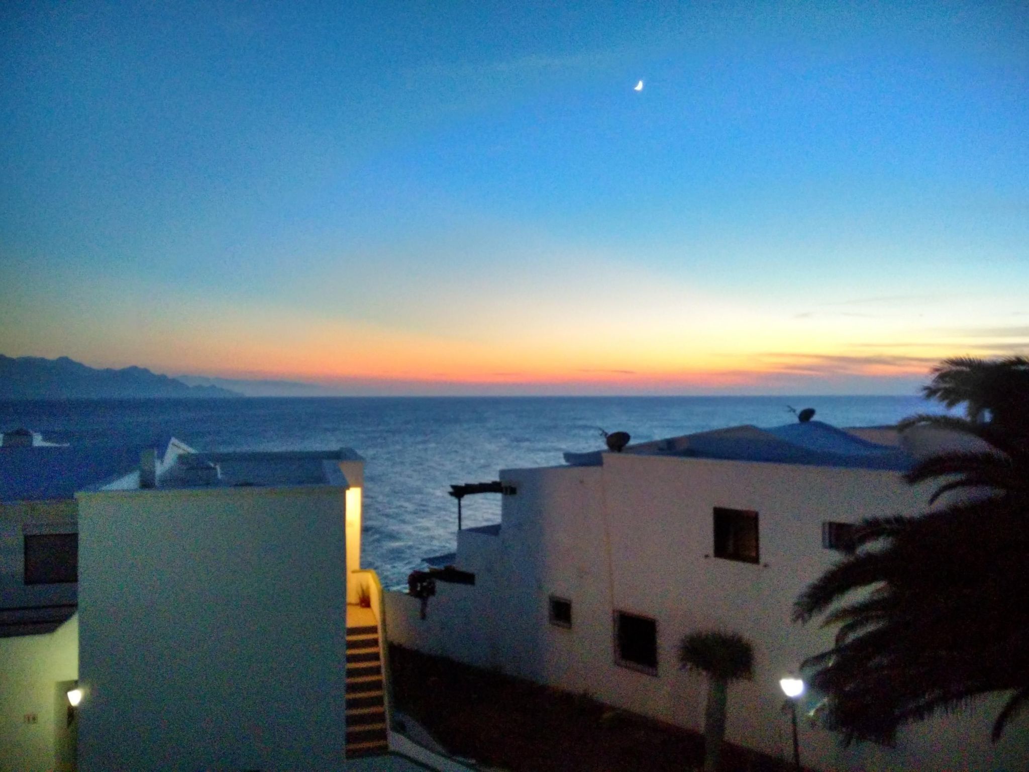 Un edificio costero con vista al mar y una luna creciente en el cielo.