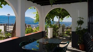 Patio esterno con tavolo e sedie in vetro, circondato da archi bianchi e vegetazione, con vista su un paesaggio suggestivo.