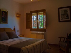 Ein Schlafzimmer mit einem Bett, einem Fenster mit Blick auf Grünflächen, einem Heizkörper und einem Sessel.