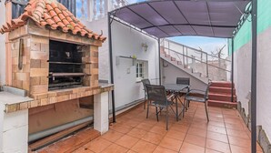 En terrasse med grill i mursten, udendørs møbler og et overdækket område.