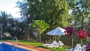 Una piscina con bordo piastrellato, circondata da una recinzione, e alcuni lettini e ombrelloni.