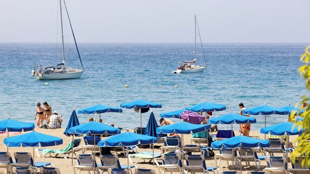 A beach with rows of blue umbrellas and lounge chairs, two sailboats in the water, and people sunbathing. - Home2Book Stylish Studio by the Sea Los Cristianos (Los Cristianos)