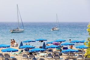 A beach with rows of blue umbrellas and lounge chairs, two sailboats in the water, and people sunbathing. - Home2Book Stylish Studio by the Sea Los Cristianos (Los Cristianos)