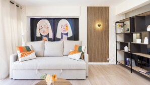 A modern living room with a sofa, a coffee table with flowers, a bookshelf, and a large abstract painting on the wall. - Home2Book Stylish Studio by the Sea Los Cristianos (Los Cristianos)