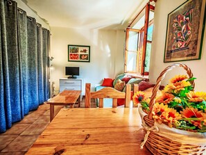 Ein gemütliches Wohnzimmer mit einem Holztisch, einem Fernseher und einem Fenster mit Blick auf Grünflächen.
