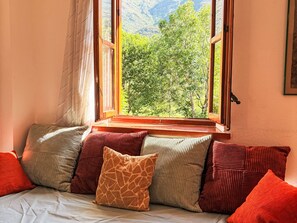 Ein Zimmer mit einem Bett, einem Fenster mit Blick auf Bäume und Berge sowie einer Wand mit einem gerahmten Bild.