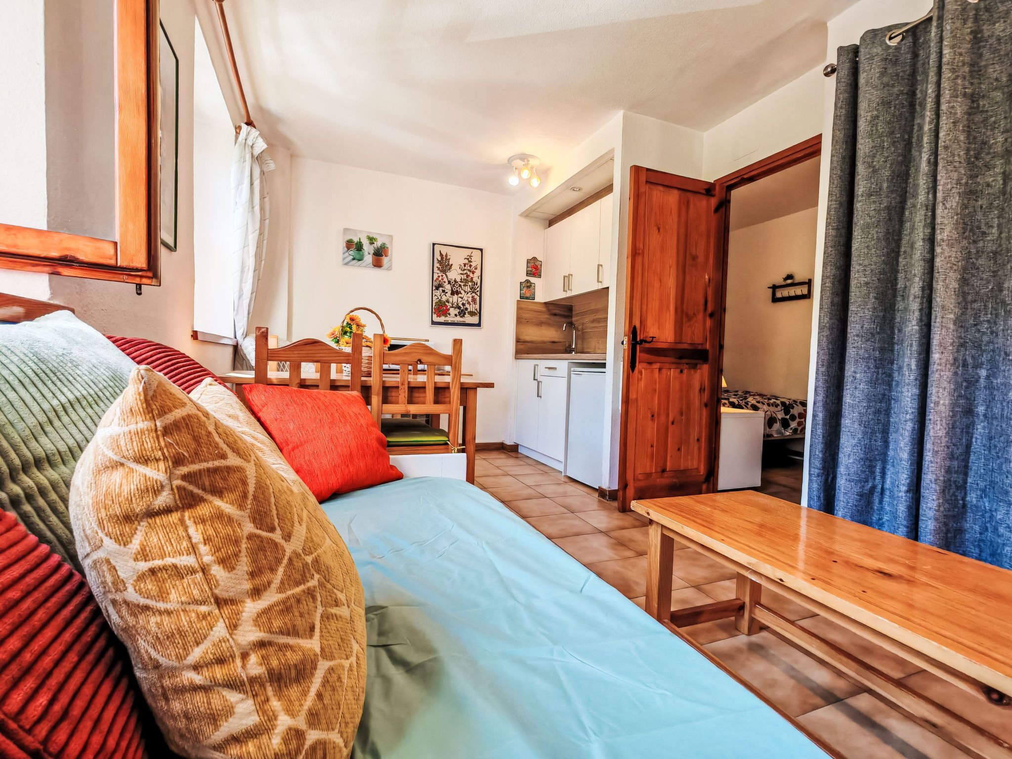 Une pièce confortable avec un lit, une table en bois, un coin cuisine et une porte donnant sur une autre pièce.