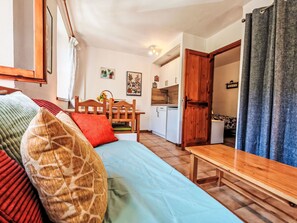 Ein gemütliches Zimmer mit einem Bett, einem Holztisch, einer Küchenzeile und einer Tür zu einem anderen Raum.