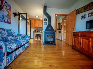 A living room with a sofa, a wooden floor, a kitchen in the background, and a fireplace. - Falcó 10 by Interhome (Caldes de Boi)