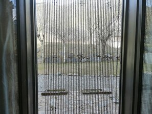 A view through a window with vertical blinds, featuring a grassy area and a few trees in the background. - Wohnung Besiberri 7 Erdgeschoss mit Terrasse Vall de Boí by Interhome (Caldes de Boi)