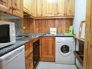 Eine kompakte Küche mit Holzausstattung, einer Mikrowelle, einer Waschmaschine und einer Arbeitsplatte aus Granit.