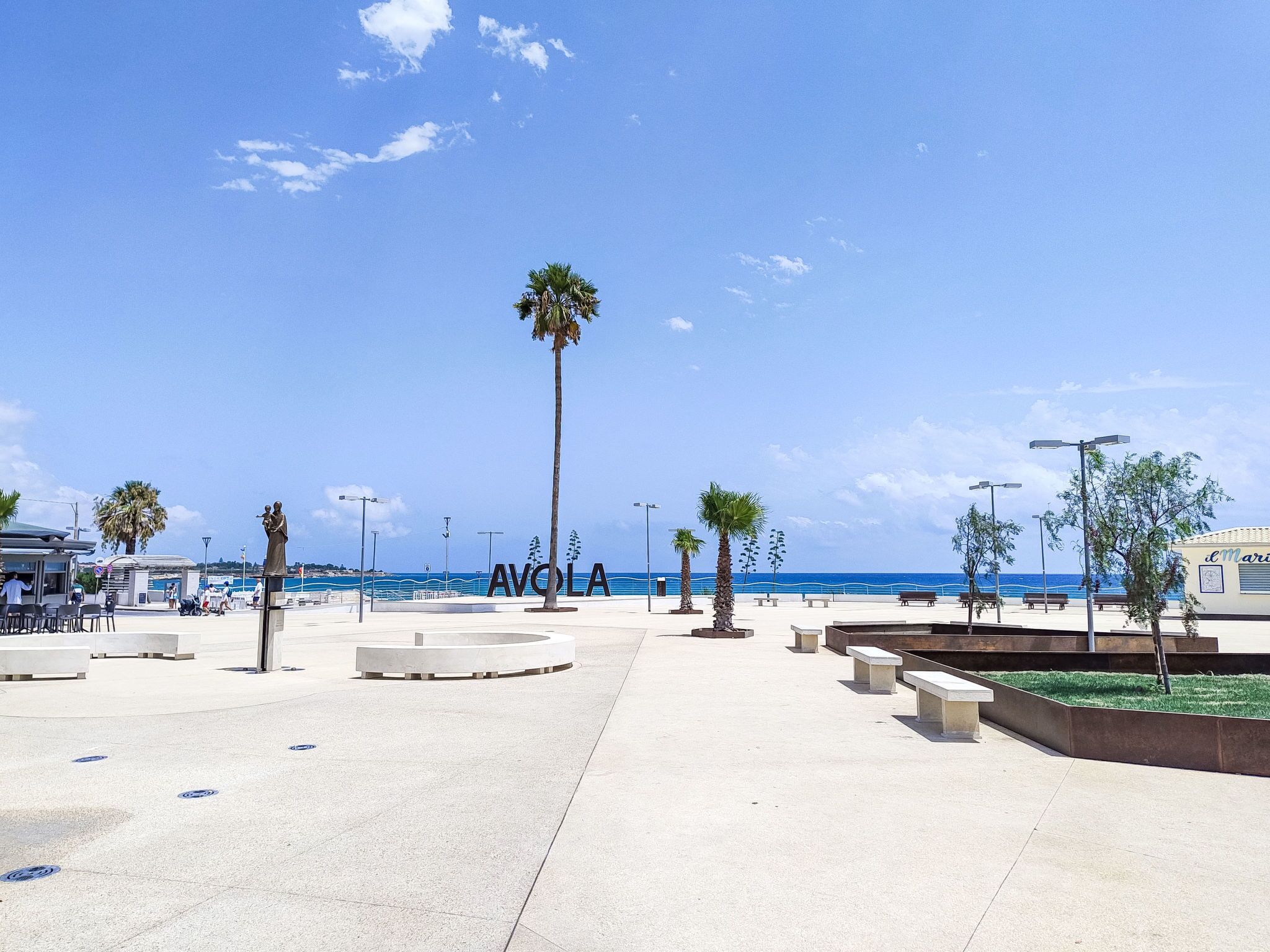 Une promenade en bord de mer, agrémentée de bancs, de palmiers et offrant une vue dégagée sur la mer.