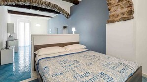 Un dormitori amb un llit, una nit, una làmpada i una paret de pedra.