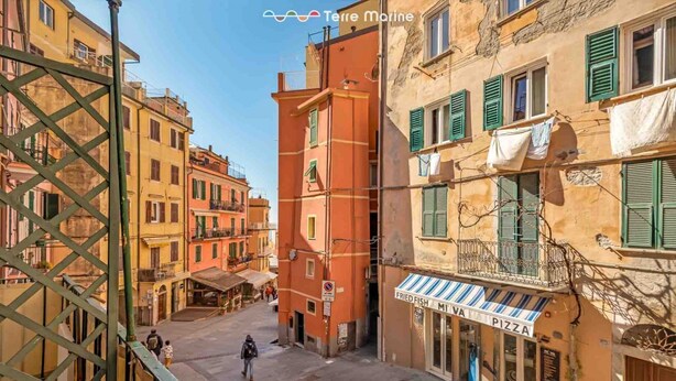 Un carrer estret amb edificis a ambdós costats, un restaurant visible anomenat 'Fried Fish Mia Pizza', i un pont per a vianants al primer pla.