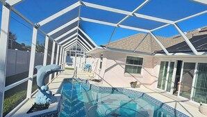 Piscina com água azul cristalina, rodeada por uma estrutura branca, e uma casa ao fundo.