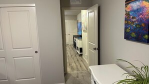 A hallway with a white door, a white bench, and a painting on the wall.
