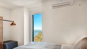 Ein Schlafzimmer mit Bett, einem kleinen Nachttisch, einem Holzschrank und einem Balkon mit Meerblick.
