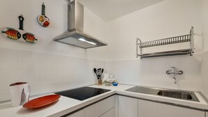 Eine moderne Küche mit weißen Schränken, einer Edelstahl-Spüle, einem eingebauten Herd und einem wandmontierten Regal.