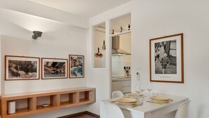 Ein Essbereich mit weißem Tisch, gedeckt für vier Personen, gerahmten Fotos an der Wand und einer Holzbank darunter.