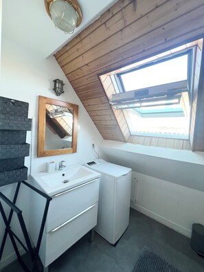 Ein kleines, modernes Badezimmer mit Oberlicht, weißem Waschbecken, Spiegel und platzsparender Wascheinrichtung.