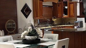 Una cucina moderna con mobili impiallacciati in legno, un'isola centrale con piano in vetro e sedie bianche attorno a un tavolo da pranzo.