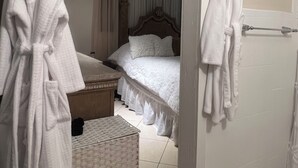Camera d'albergo con un letto, una testiera in legno, un tappetino da bagno bianco e due accappatoi bianchi appesi a ganci.