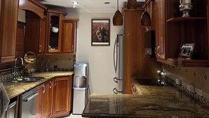 Una cucina con mobili in legno, un frigorifero in acciaio inossidabile, un dispenser di acqua e lampade a sospensione.