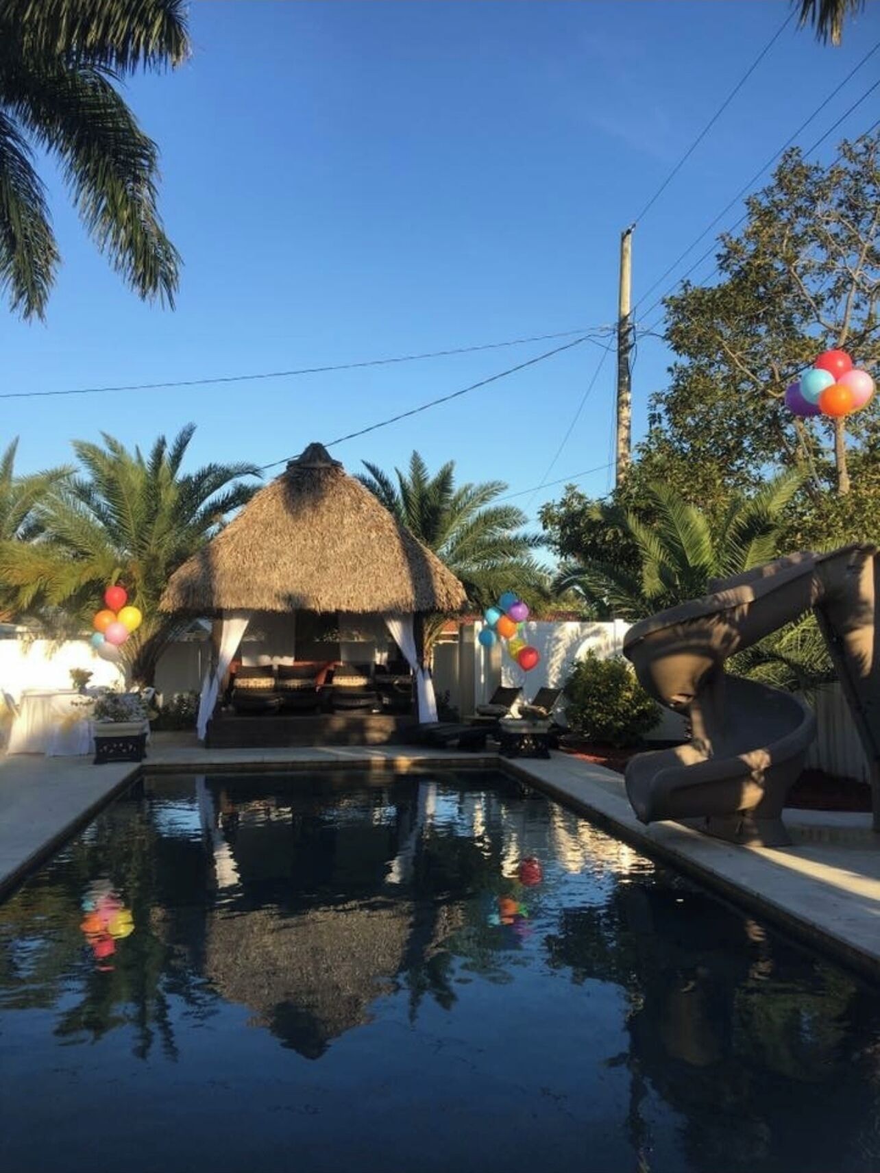 A pool area with a thatched-roof structure, lounge chairs, and a clear blue sky.