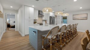 A modern kitchen with white cabinetry, a large island with bar stools, and pendant lighting. - Seashellin' - Short walk to beach (Panama City Beach)