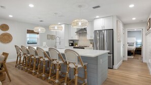 A modern kitchen with a central island, bar stools, stainless steel appliances, and pendant lighting. - Seashellin' - Short walk to beach (Panama City Beach)